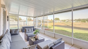 A covered outdoor seating area with a sofa, chairs, and a small table, overlooking a sports field. - 6 Mi to Disney World: Home w/ Large Yard! (Kissimmee)