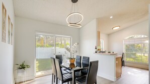 A modern dining area with a glass table, black chairs, and a hanging light fixture. - 6 Mi to Disney World: Home w/ Large Yard! (Kissimmee)