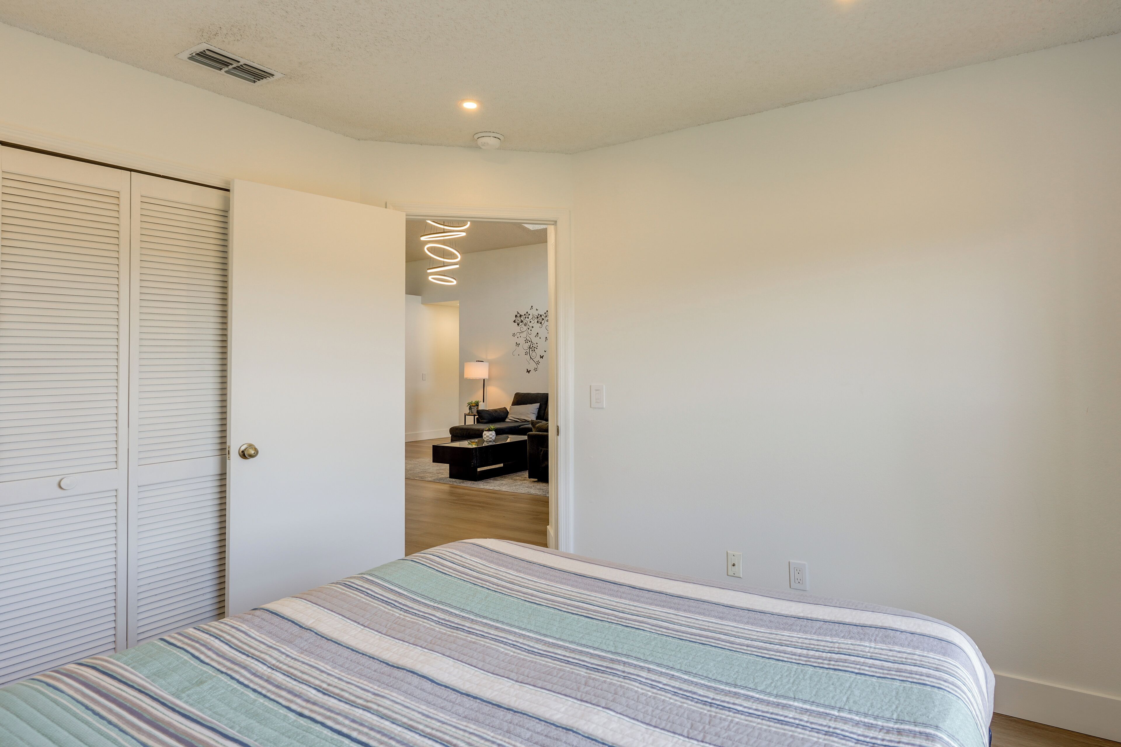 A bedroom with a bed, a wardrobe, and a hallway leading to a living area.