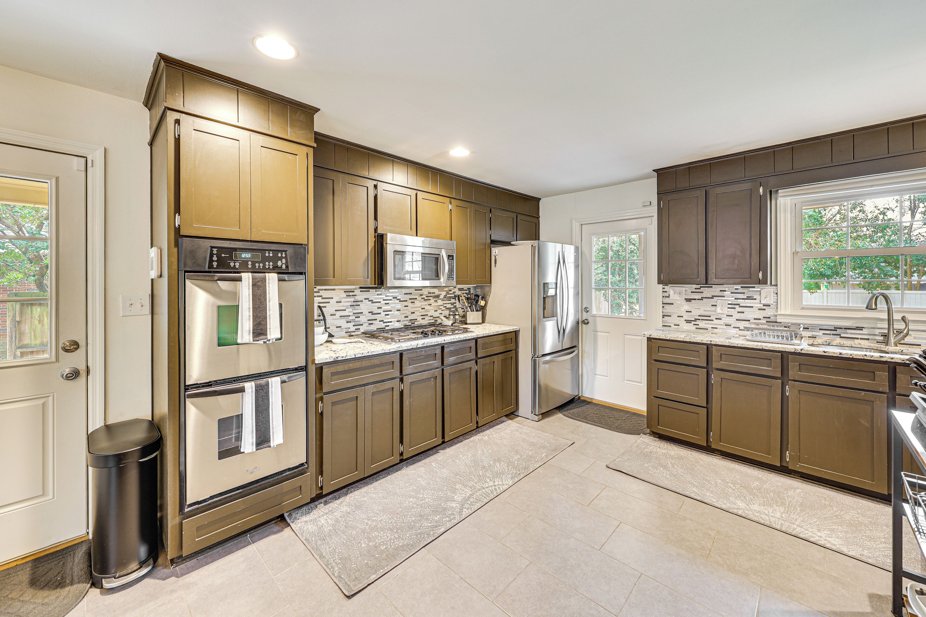 A modern kitchen with stainless steel appliances, wooden cabinets, and a large window providing natural light.