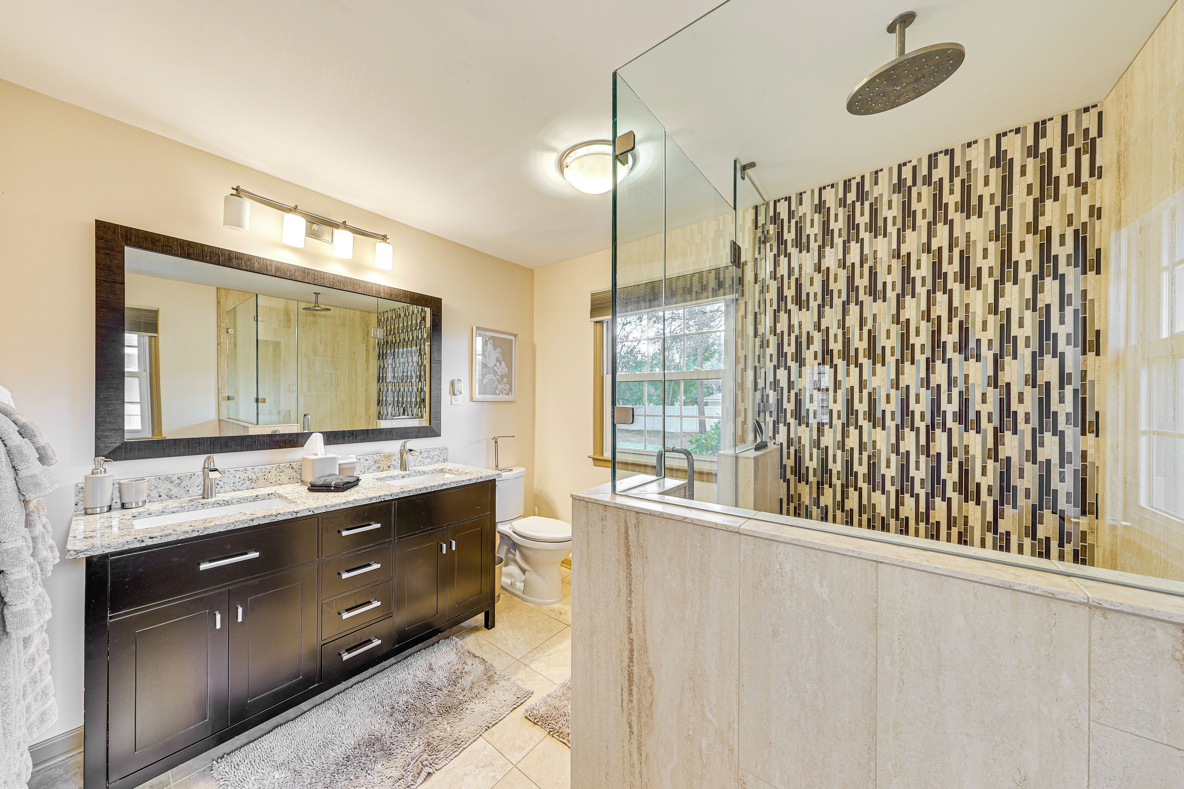 A modern bathroom with a large mirror, dark cabinetry, a shower with a glass enclosure, and a patterned tile wall.