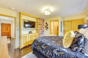 Un dormitorio con una cama grande, un televisor en un estante, una pared de ladrillo y una puerta de madera.