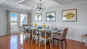 A dining area with a large table, multiple chairs, a chandelier, and framed fish illustrations on the wall. - Luxurious Oceanfront Home w/ Soaring Views + Private Pool by Tybee Cottages (Tybee Island)