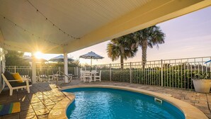 A swimming pool with a tiled deck, surrounded by a white fence, and outdoor furniture including chairs and a table. - Luxurious Oceanfront Home w/ Soaring Views + Private Pool by Tybee Cottages (Tybee Island)