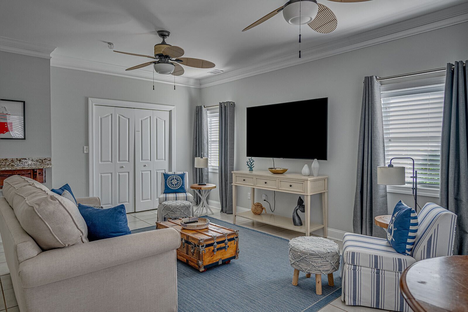 A living room with a sofa, armchair, ottoman, coffee table, TV, and a ceiling fan.