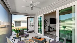Un patio moderno con muebles de mimbre, un ventilador de techo y vistas del barrio.