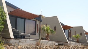 A modern hotel with a flat roof, large windows, and a balcony with a chair and potted plants. - Reva Miami Hotel Restaurant SPA (Foça)
