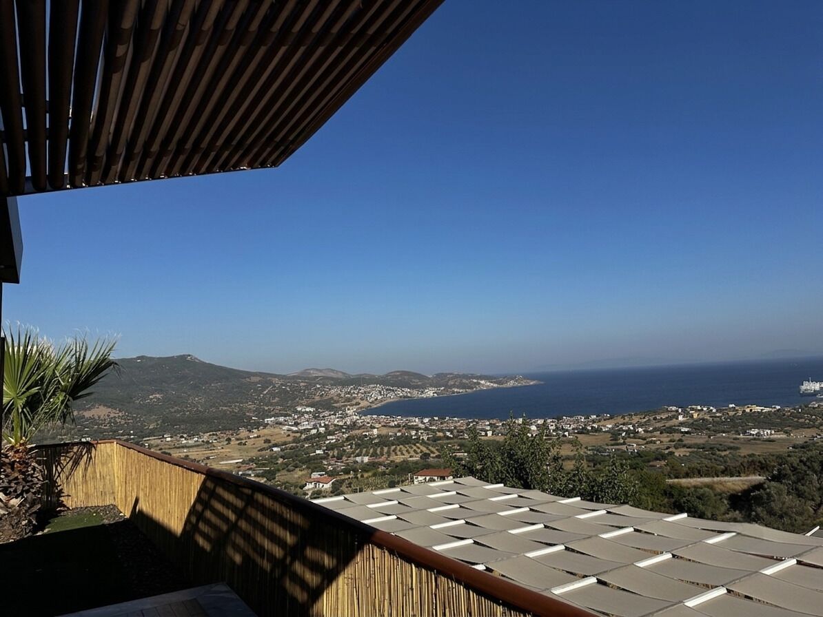 A view from a balcony with a clear sky, overlooking a coastal landscape with buildings and hills.