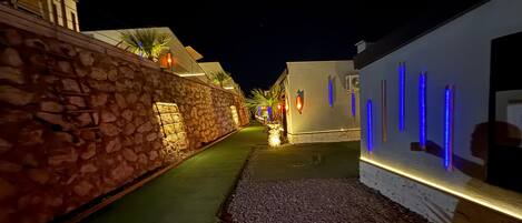 A nighttime street with stone walls, a paved path, and illuminated blue vertical lights.