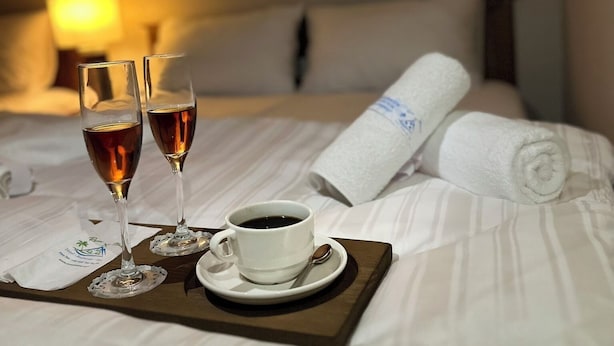 A neatly made bed with a rolled towel, two glasses of a dark beverage, and a cup of coffee on a tray. - Reva Miami Hotel Restaurant SPA (Foça)