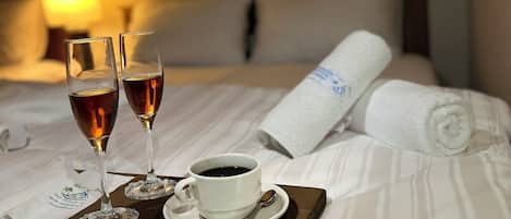 A neatly made bed with a rolled towel, two glasses of a dark beverage, and a cup of coffee on a tray.