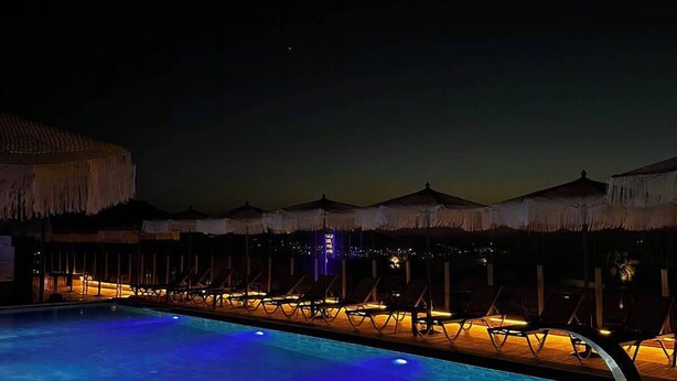 A nighttime pool area with lounge chairs and umbrellas. - Reva Miami Hotel Restaurant SPA (Foça)
