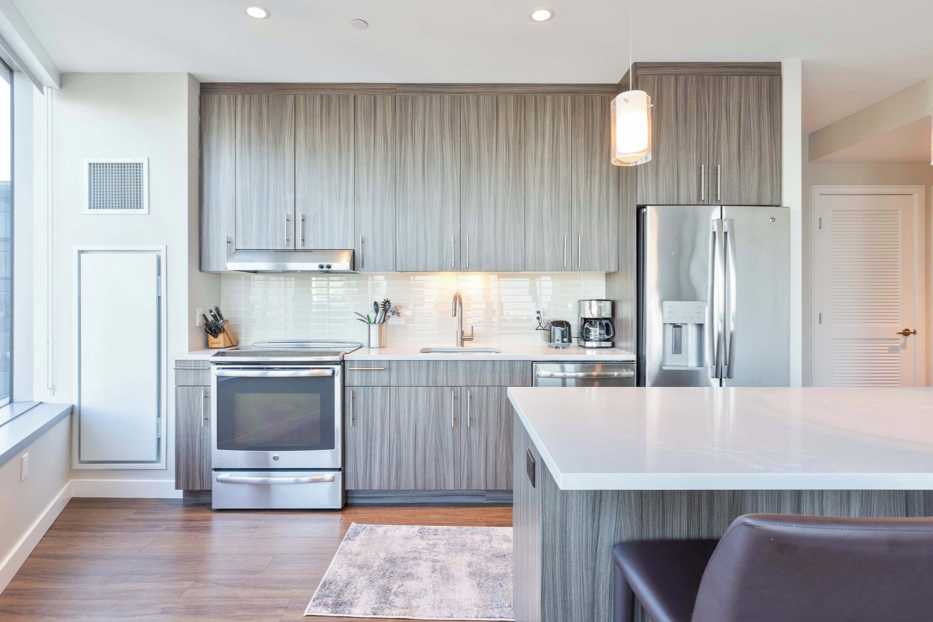 A modern kitchen with grey cabinetry, stainless steel appliances, and a central island.