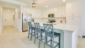 A modern kitchen with white cabinetry, a central island with bar stools, stainless steel appliances, and pendant lighting. - Ibis Landing Golf Club On-site: Condo w/ Porch! (Lehigh Acres)