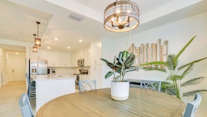 A modern kitchen with white cabinets, stainless steel appliances, and a wooden dining table with chairs. - Ibis Landing Golf Club On-site: Condo w/ Porch! (Lehigh Acres)