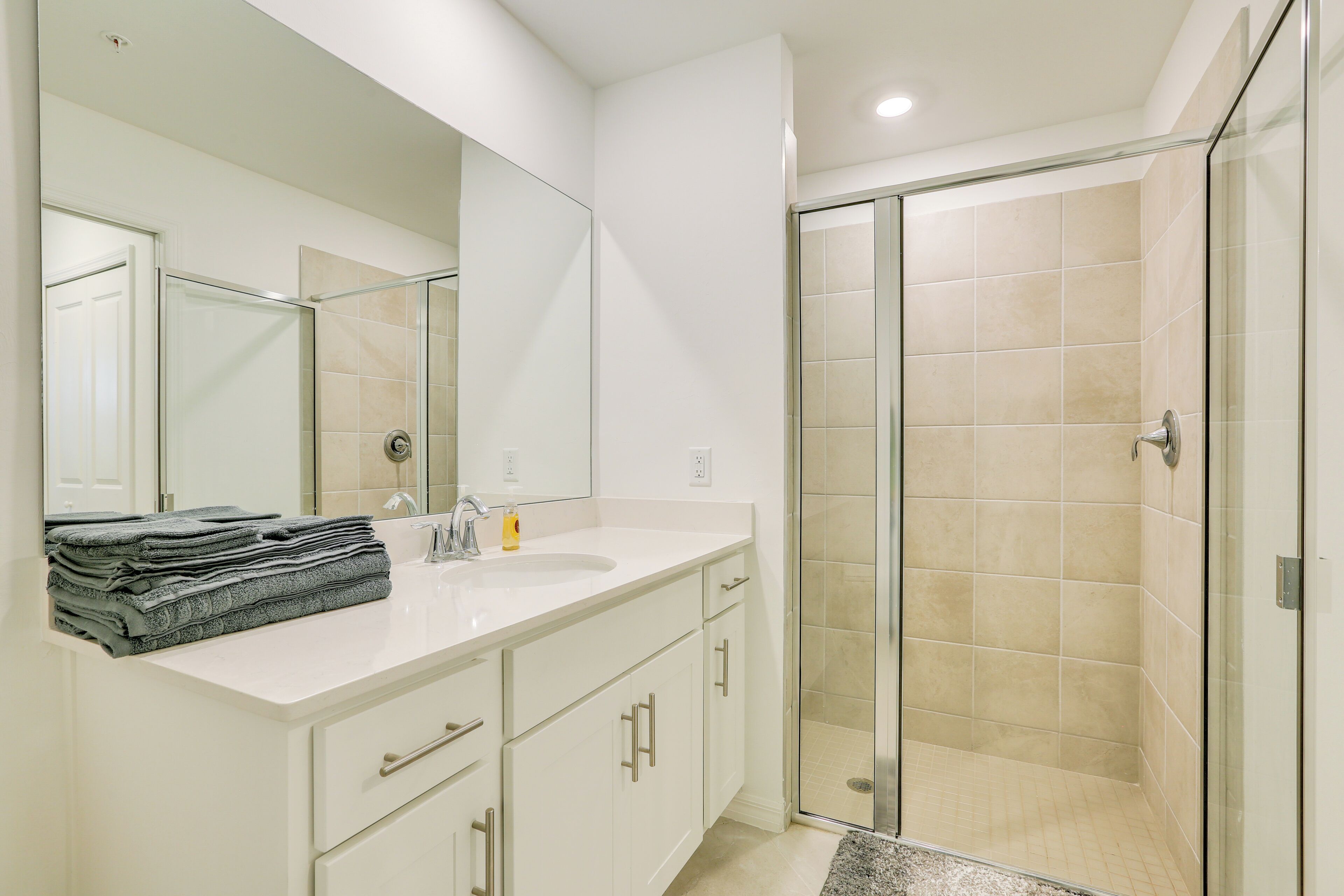 Une salle de bain moderne avec un meuble-lavabo blanc, un grand miroir et une douche à parois de verre.