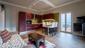 A modern kitchen with red cabinets, a dining area with white chairs, and a balcony with a view.