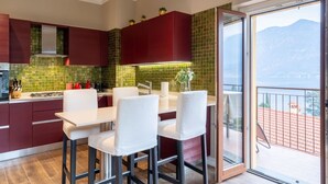 A modern kitchen with red cabinets, a white dining area, and a view of mountains through a glass door.