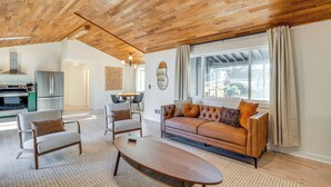 A spacious living room with a wooden ceiling, a sofa set, a coffee table, and a kitchen area in the background. - Modern Oregon Cottage w/ Hot Tub: Walk to Beach! (Cloverdale)