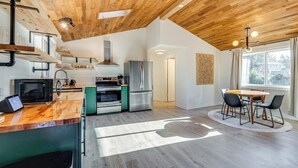 A modern kitchen with wooden ceiling, stainless steel appliances, and a dining area with a round table and chairs. - Modern Oregon Cottage w/ Hot Tub: Walk to Beach! (Cloverdale)