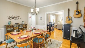 A dining area with a wooden table set for four, flanked by chairs with blue cushions, a chandelier above, and a piano to the right. - Game Day Base! 1 Mi to Ole Miss & Downtown (Oxford)