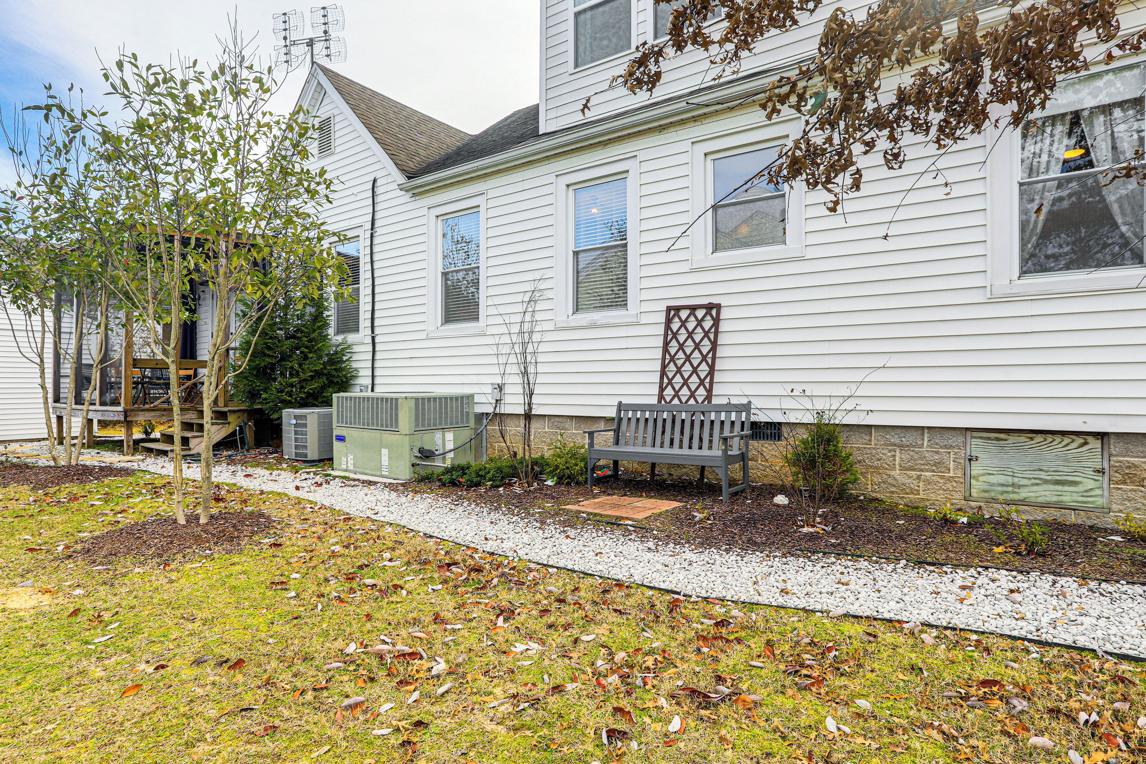 A white two-story house with a front porch, a bench, and a small tree.