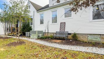 A white two-story house with a front porch, a bench, and a small tree.
