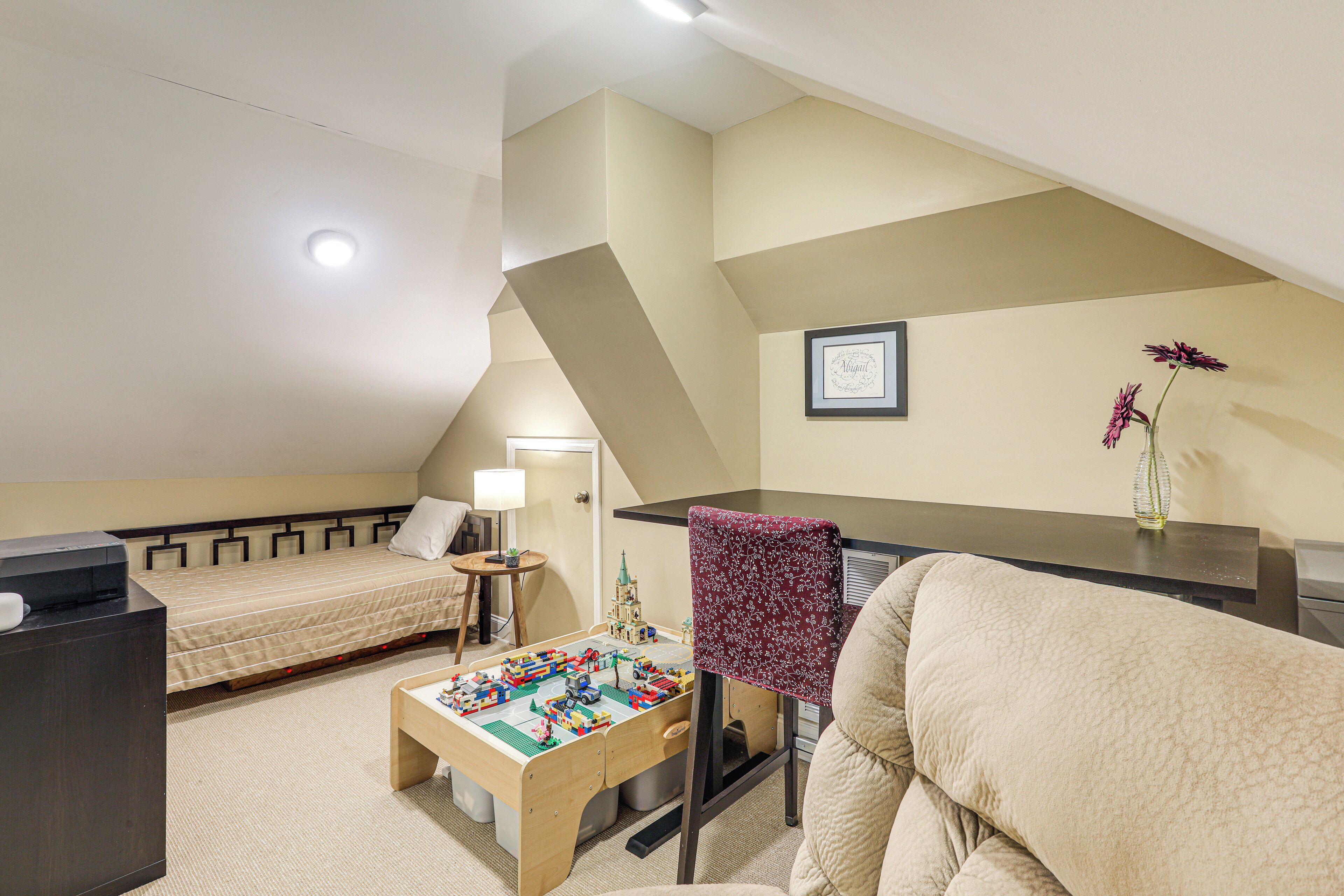 Une pièce comprenant un lit, un bureau, une chaise, une petite table avec des jouets et un tableau encadré accroché au mur.