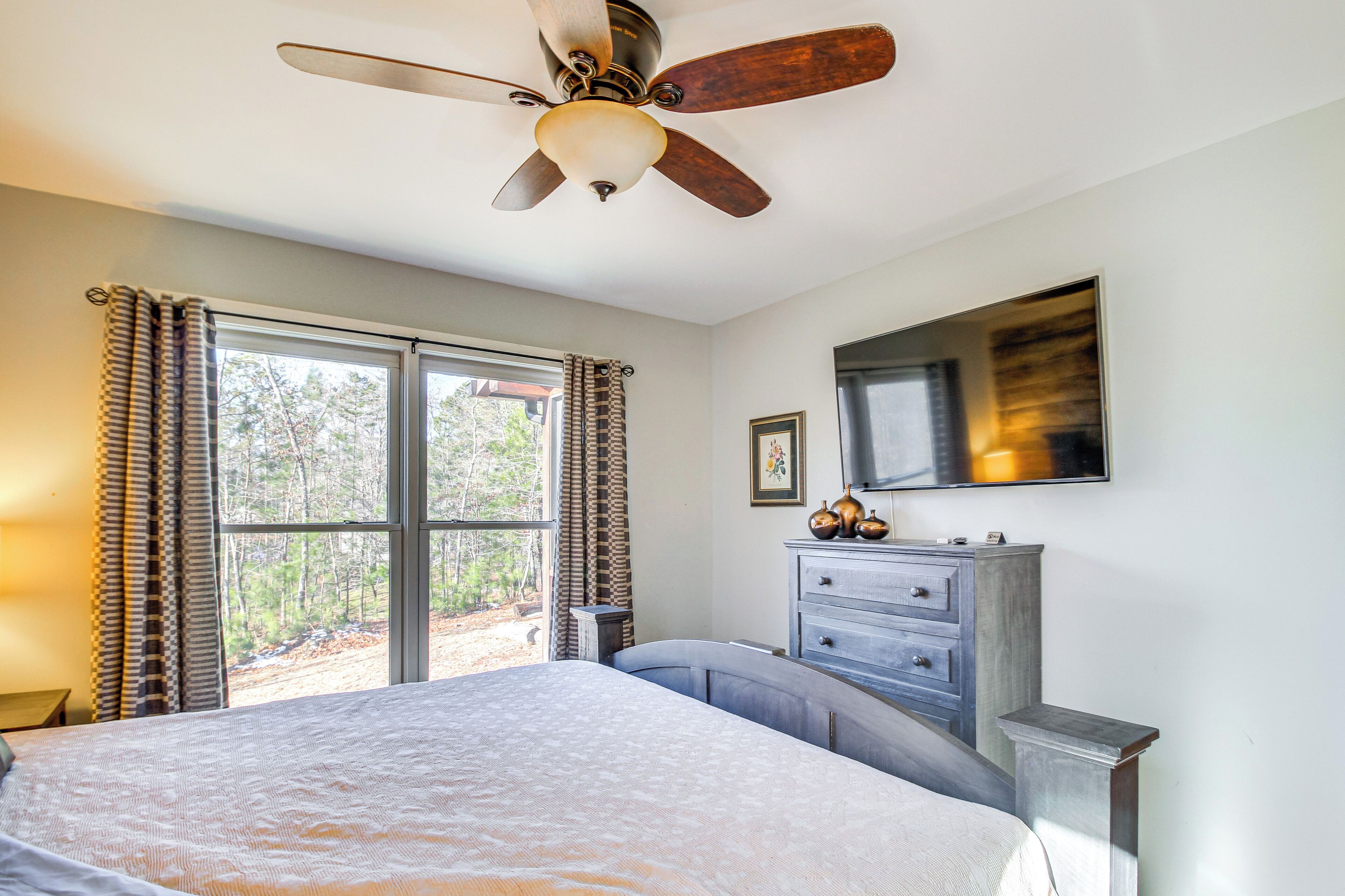 A bedroom with a bed, a ceiling fan, a dresser, and a window with curtains.