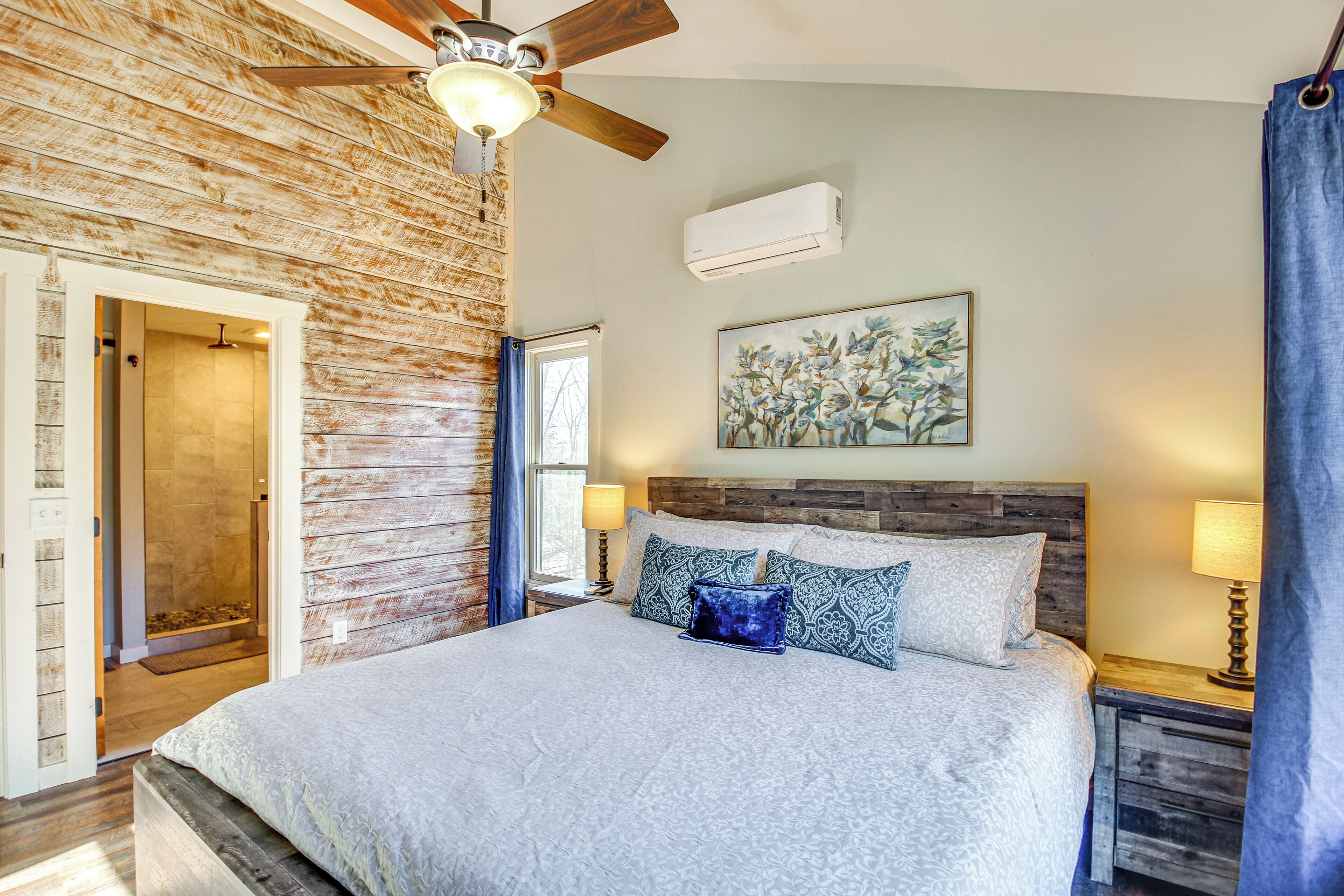 A bedroom with a wooden headboard, a large bed with patterned bedding, two bedside lamps, and a ceiling fan.