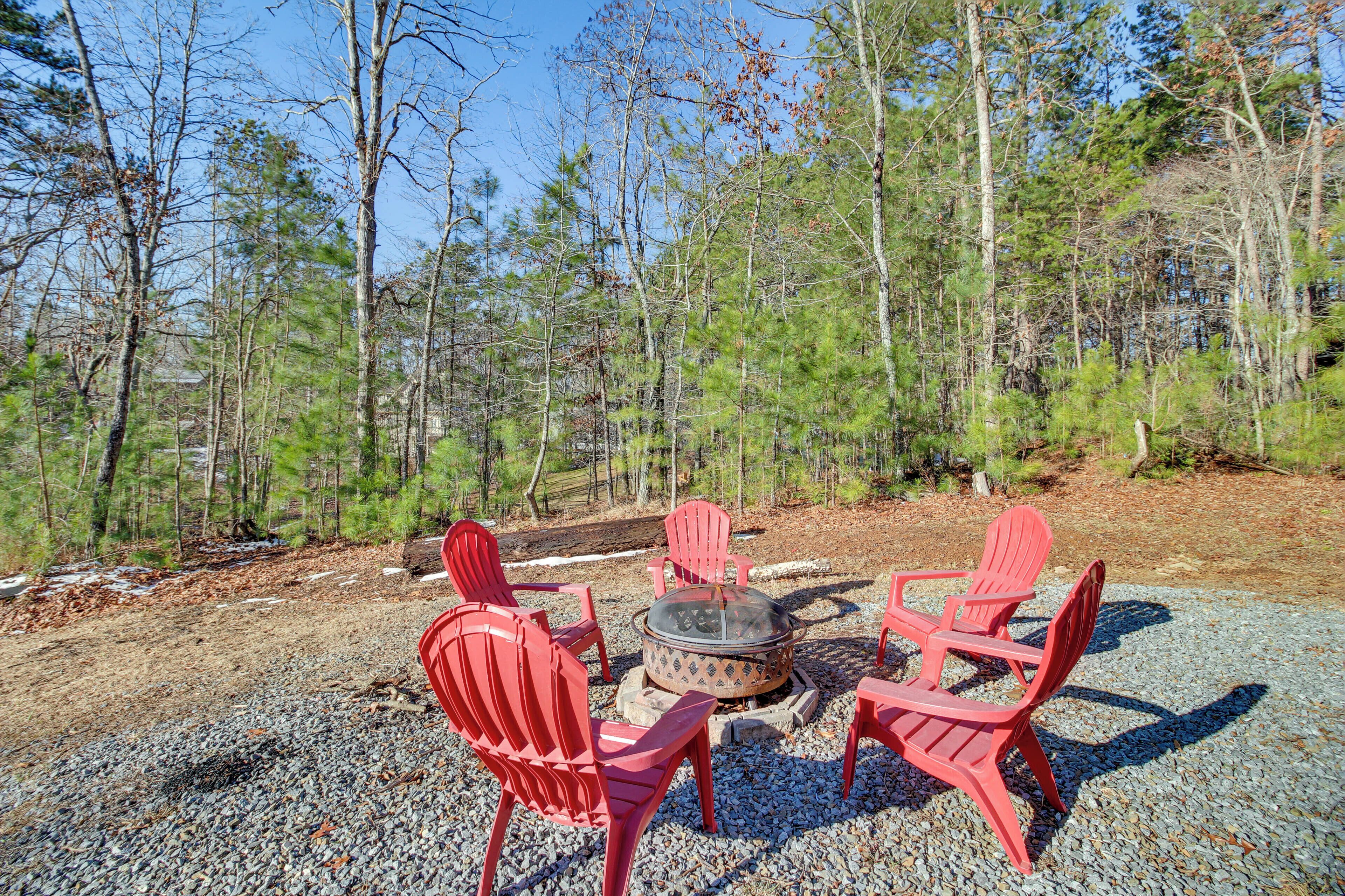 Un foyer entouré de chaises Adirondack rouges, installé sur une surface de gravier avec des arbres en arrière-plan.