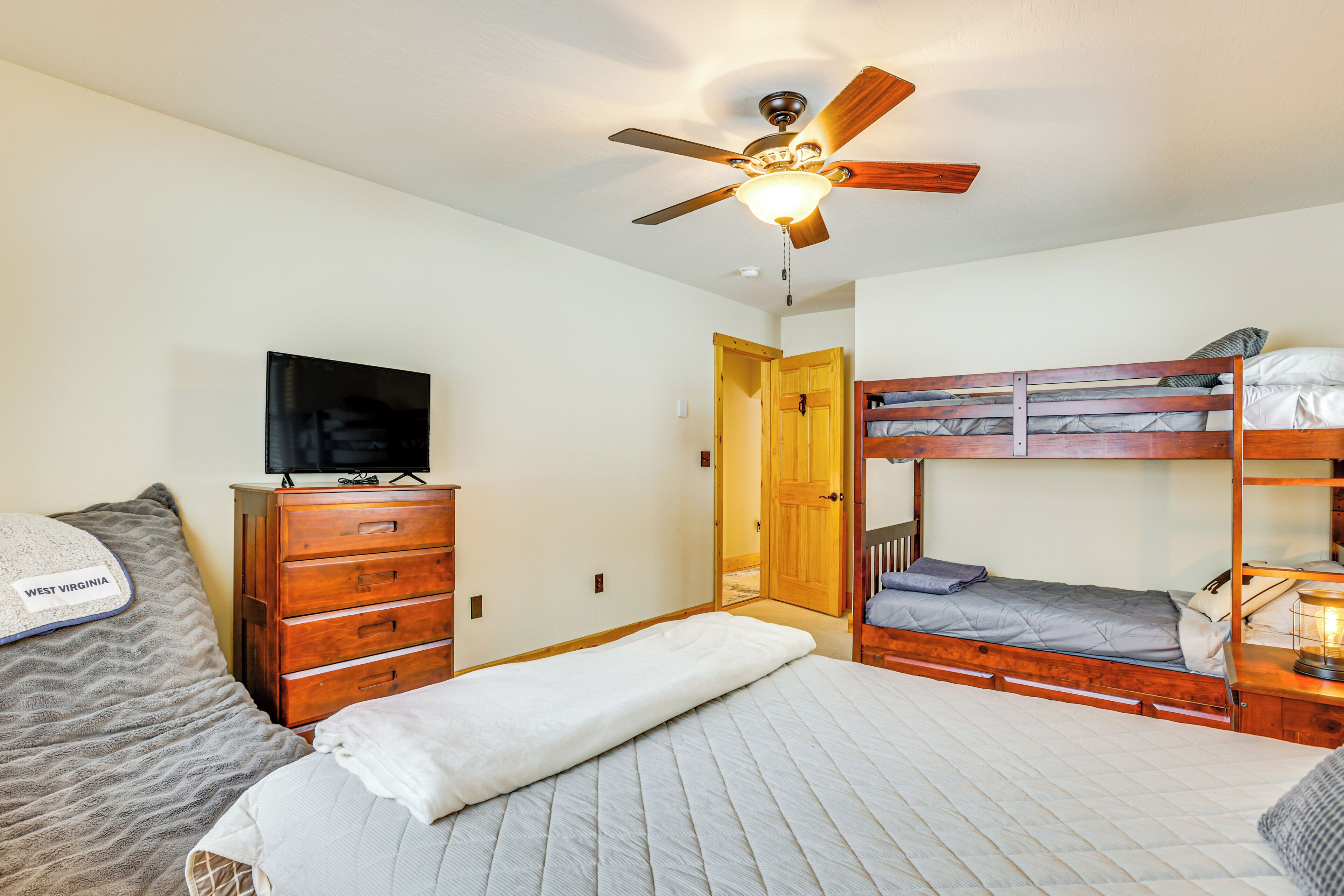 A bedroom with a single bed, a dresser, a television, a ceiling fan, and a bunk bed.