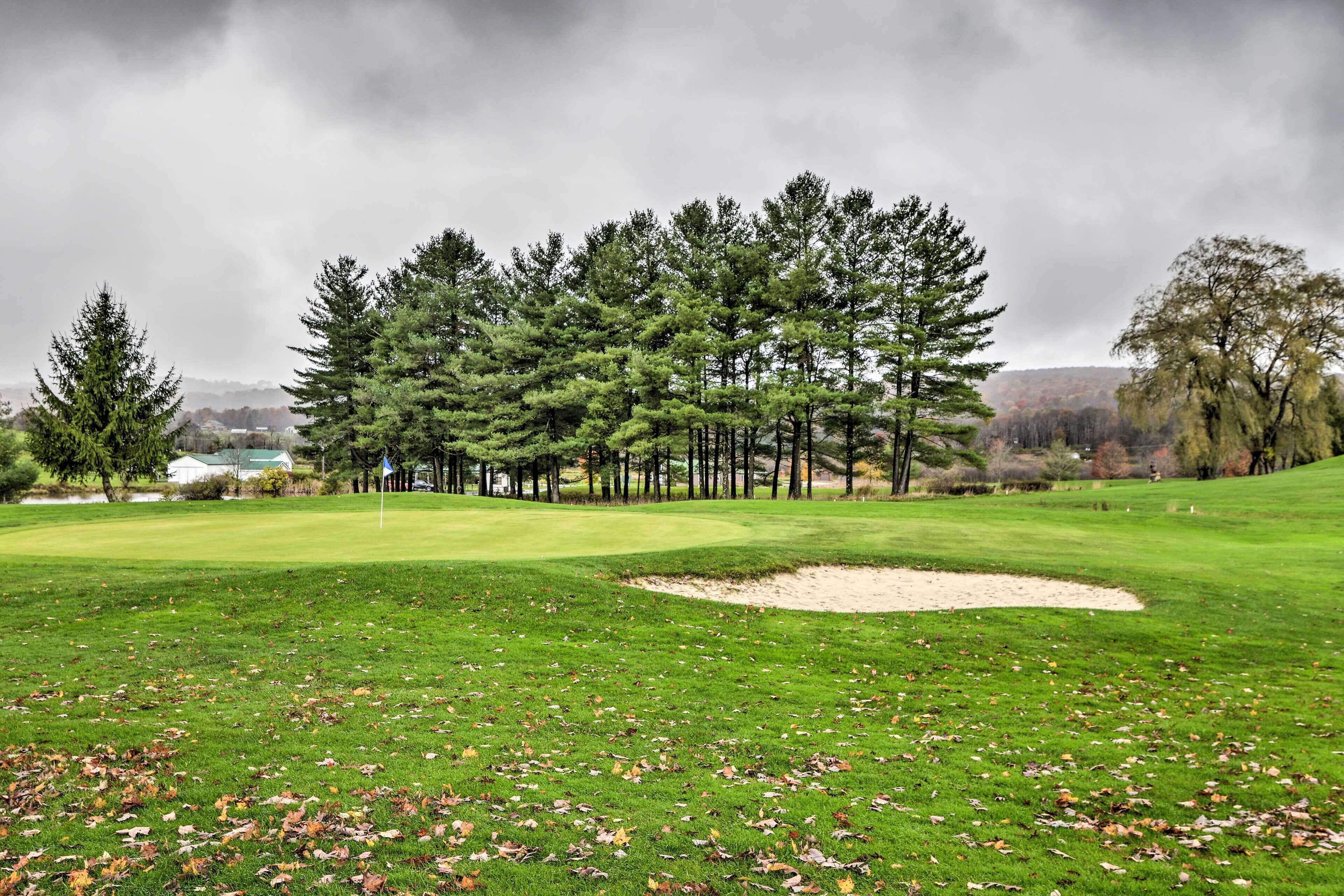 A golf course with a sand bunker, trees, and a cloudy sky.