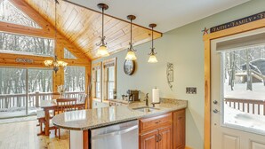 Une cuisine dotée d’un plan de travail en granit, de meubles en bois, d’un lave-vaisselle en acier inoxydable et d’une grande fenêtre donnant sur une terrasse enneigée.