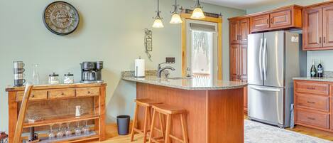 Una cocina con armarios de madera, un refrigerador de acero inoxidable, una barra de bar con taburetes y un reloj en la pared.