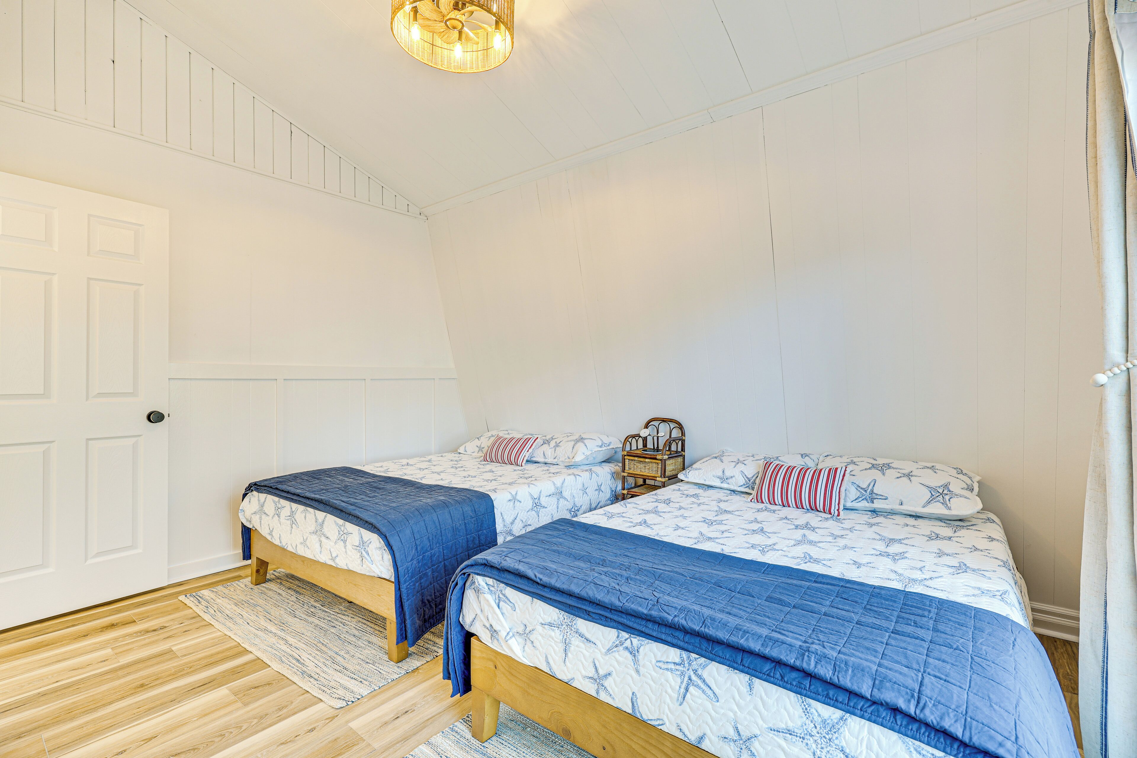 A bedroom with two beds, a wooden floor, a white door, and a ceiling light fixture.