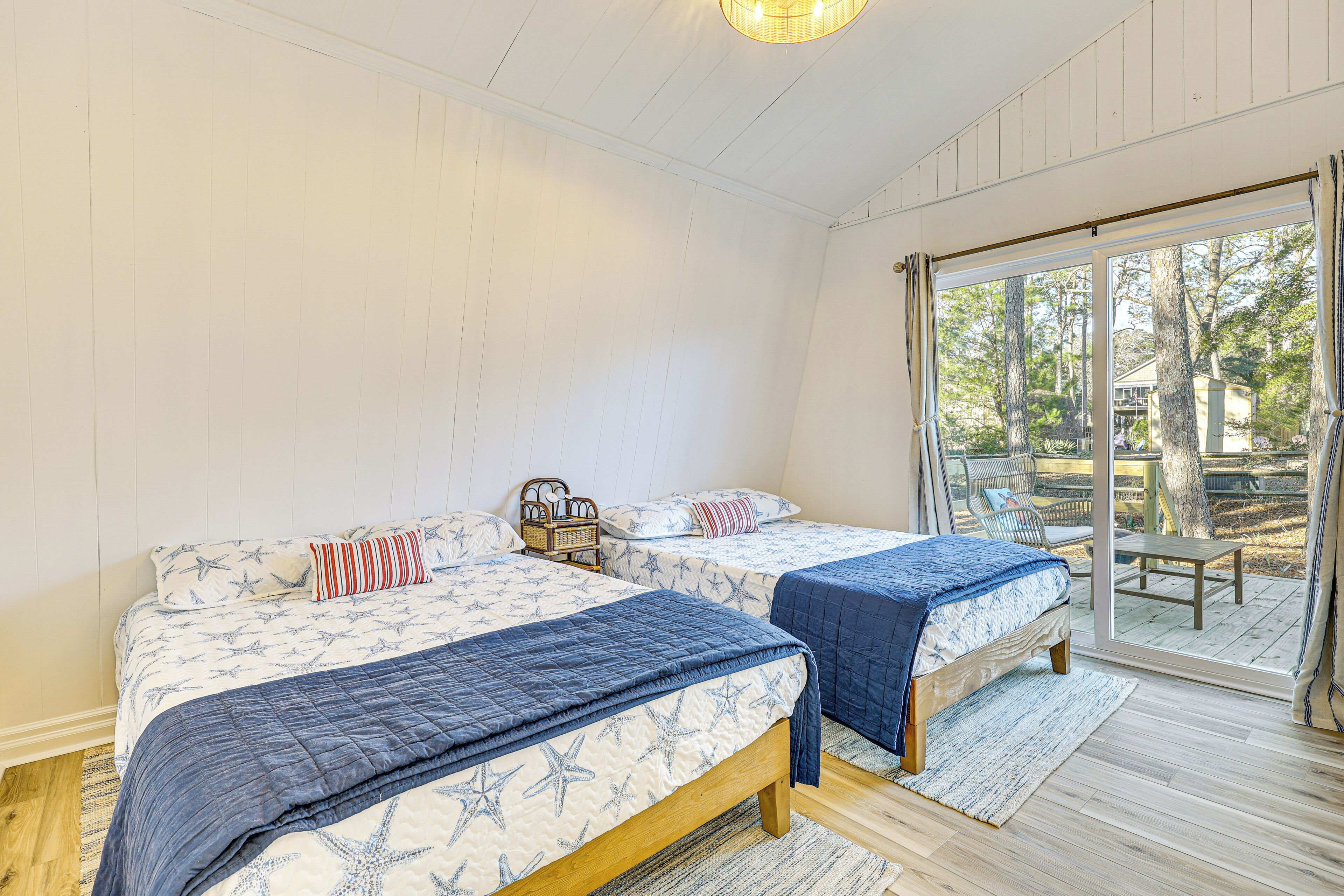 A bedroom with two beds, a wooden floor, and a large sliding glass door leading to an outdoor deck.