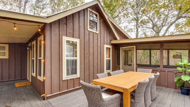 A wooden deck with a wooden table and wicker chairs, surrounded by a wooden building with windows and a door.