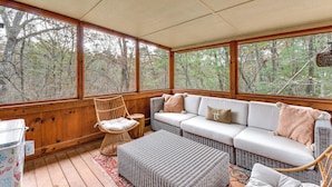 A covered porch with a wicker sofa, a wooden chair, and a small table.