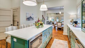 Une cuisine spacieuse avec un grand îlot central, un plancher en bois et des luminaires suspendus.