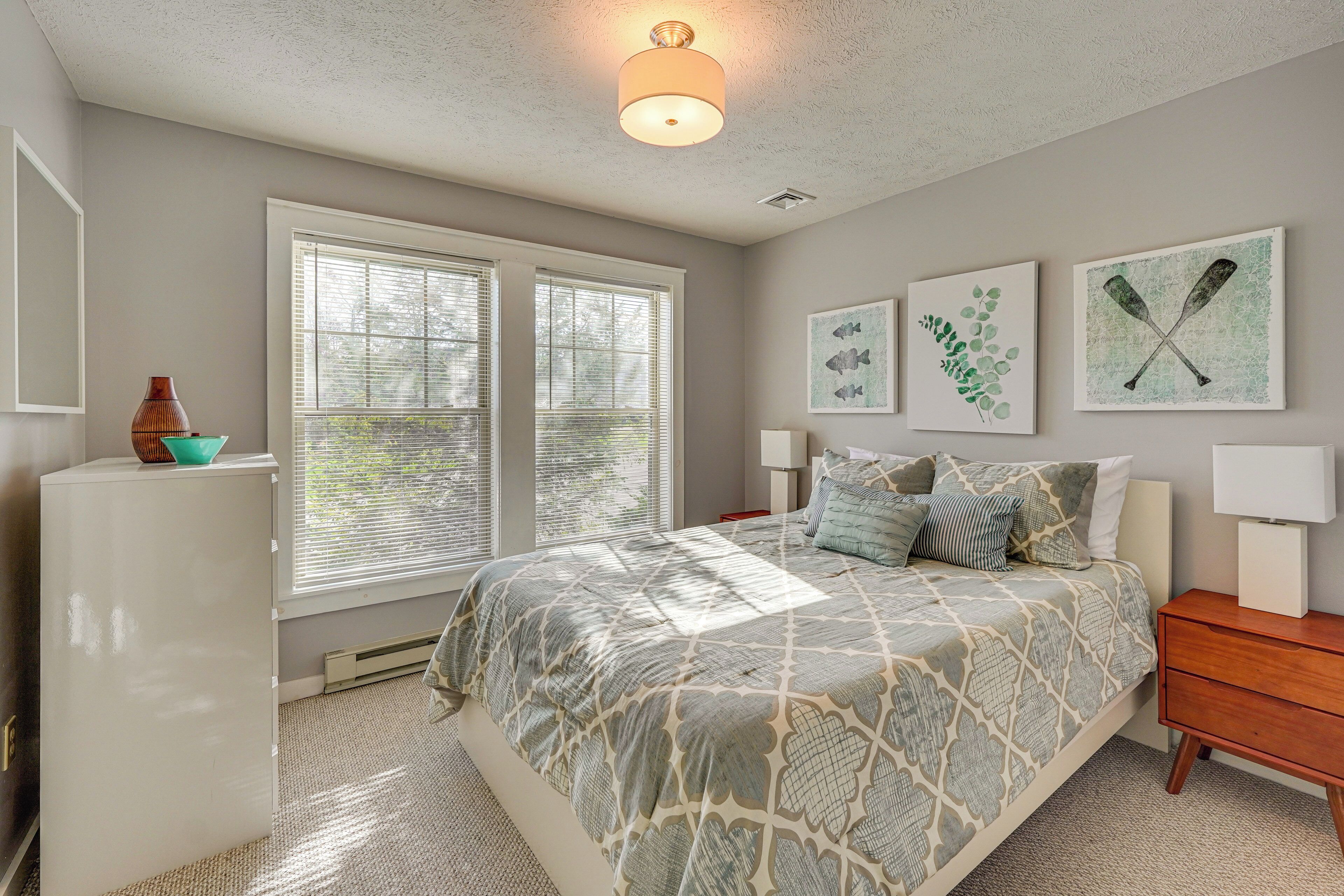 A bedroom with a bed, a dresser, a window, and wall art.
