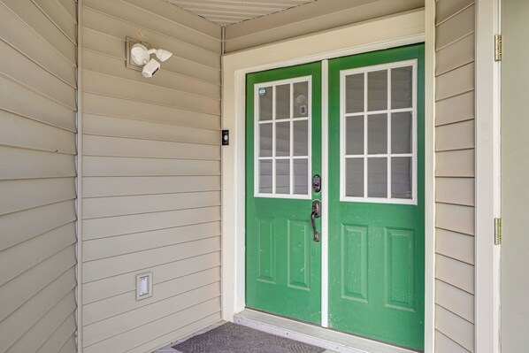 Uma porta verde com moldura branca, um tapete de entrada e uma luminária fixada na parede.