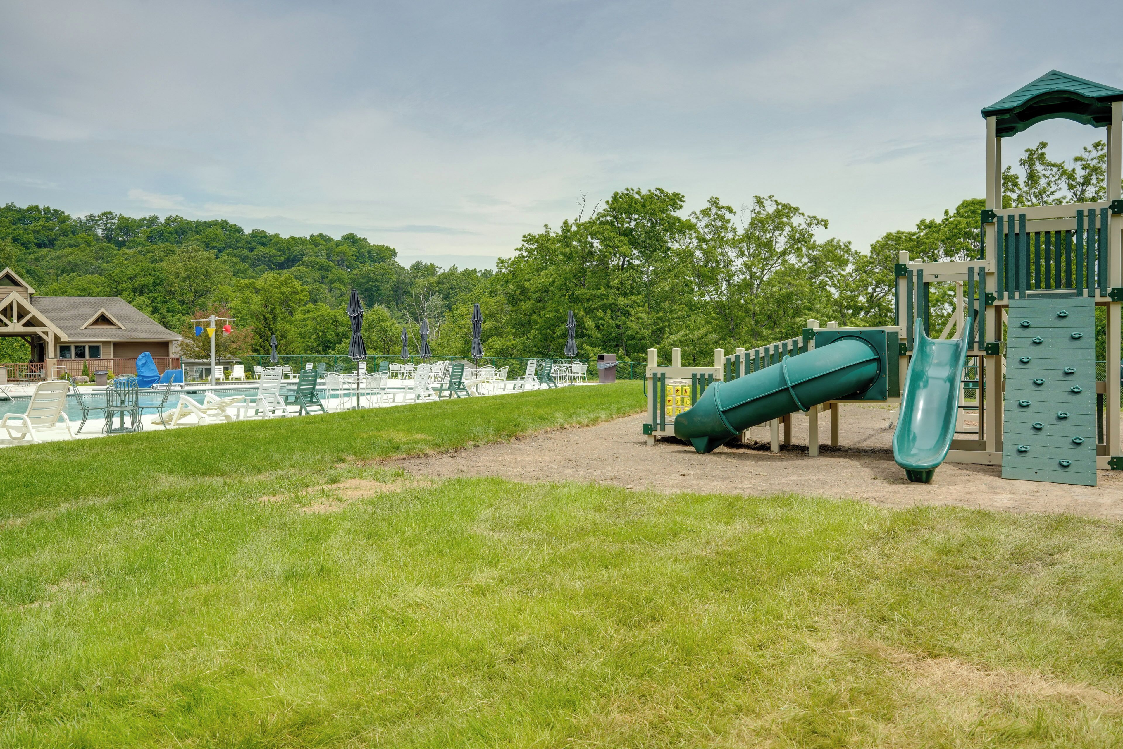 A playground with slides and climbing structures, a pool area with lounge chairs, and a building with a pitched roof.