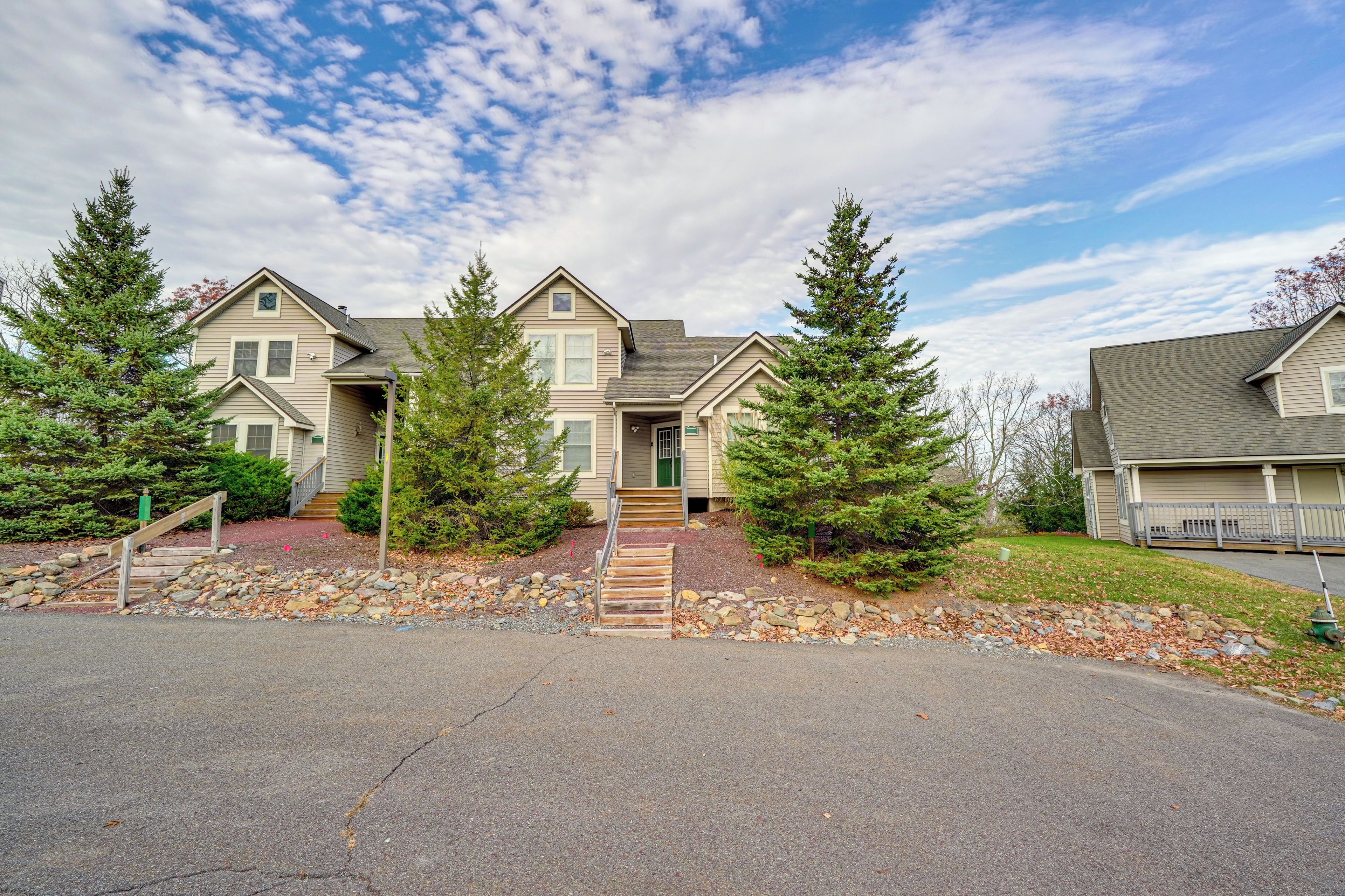 A two-story residential building with a front entrance, a stone pathway leading to the door, and a small porch area.