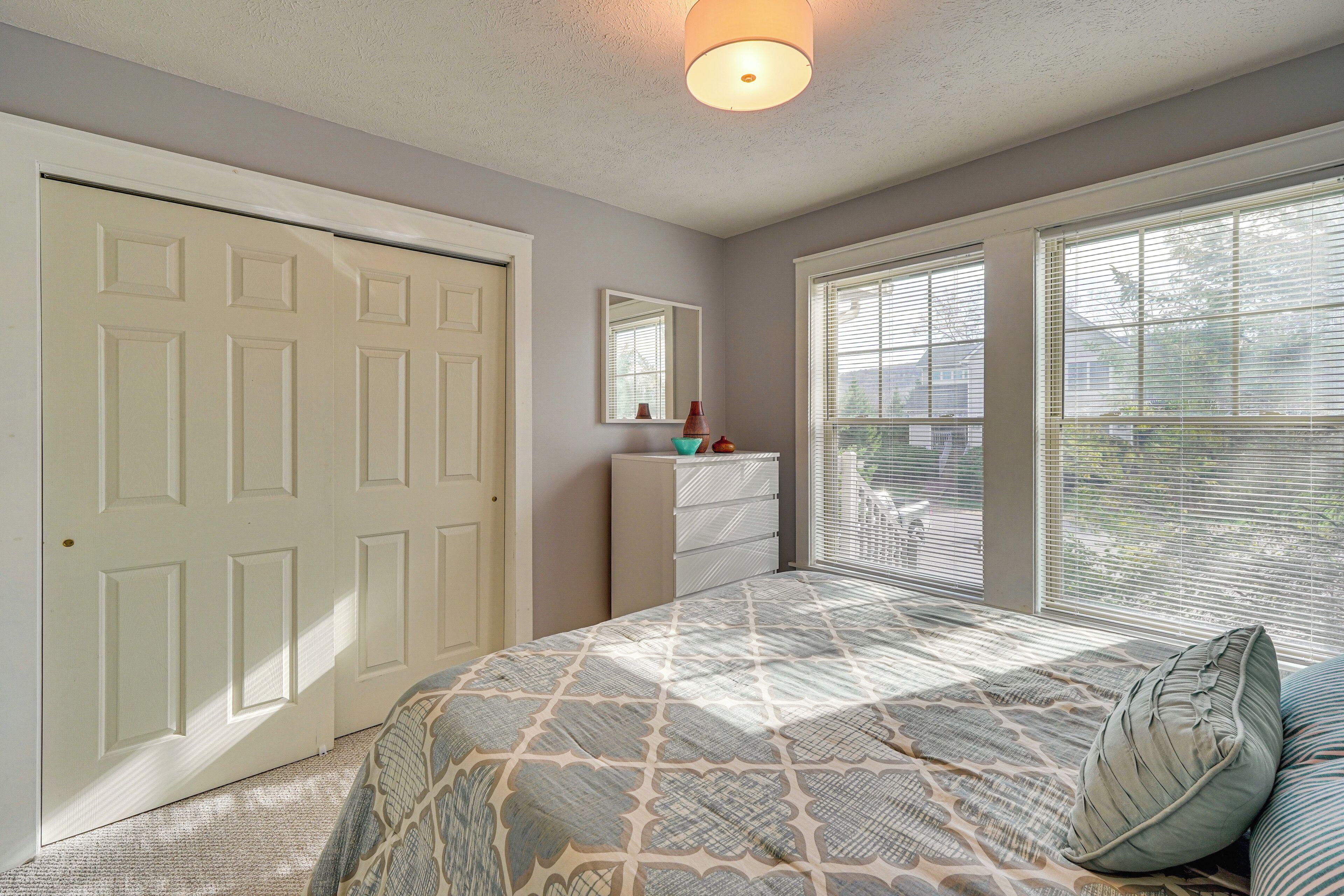 A bedroom with a bed, dresser, and large windows.