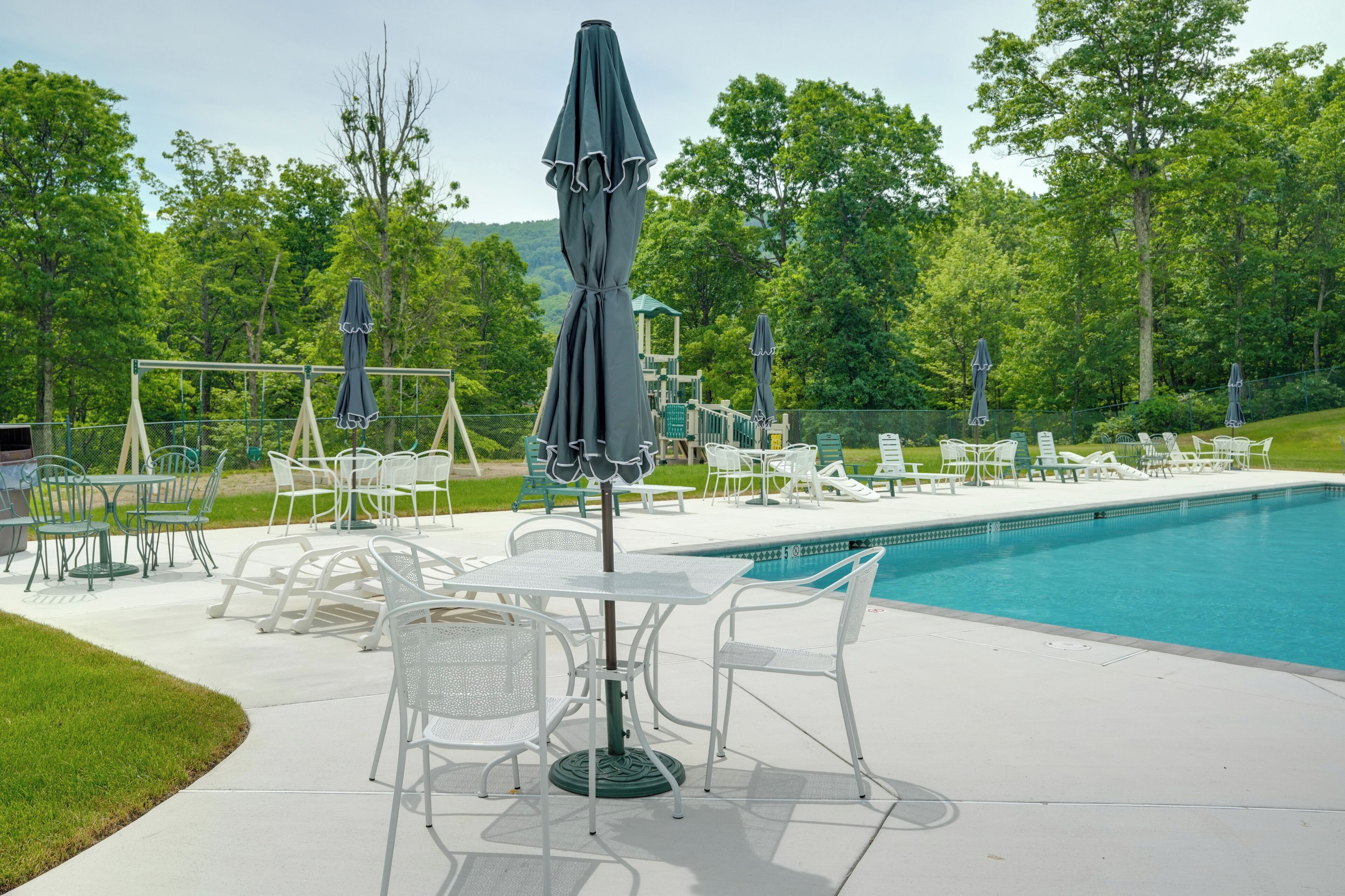 A poolside area with white tables and chairs, umbrellas, and a clear blue pool.