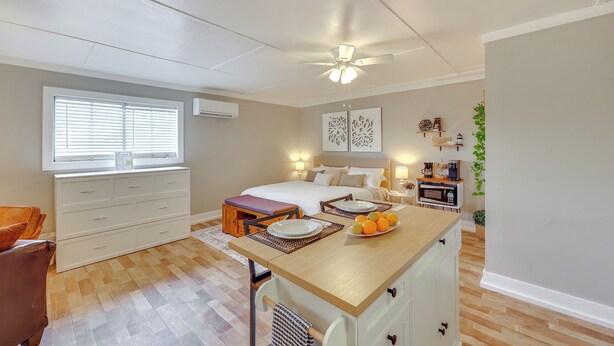 Une chambre à coucher comprenant un lit, des tables de chevet, un bureau, une chaise, une fenêtre et un ventilateur de plafond.