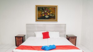 A neatly made bed with a red and white bedspread, a blue towel, and a painting above it. There are two wooden nightstands with drawers, one on each side of the bed. -  Villa CHR Syariah (Banjarbaru)