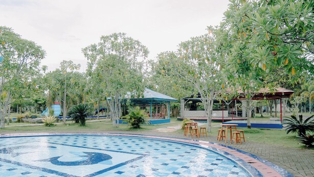 A swimming pool with a checkered pattern, surrounded by trees and a gazebo. -  Villa CHR Syariah (Banjarbaru)
