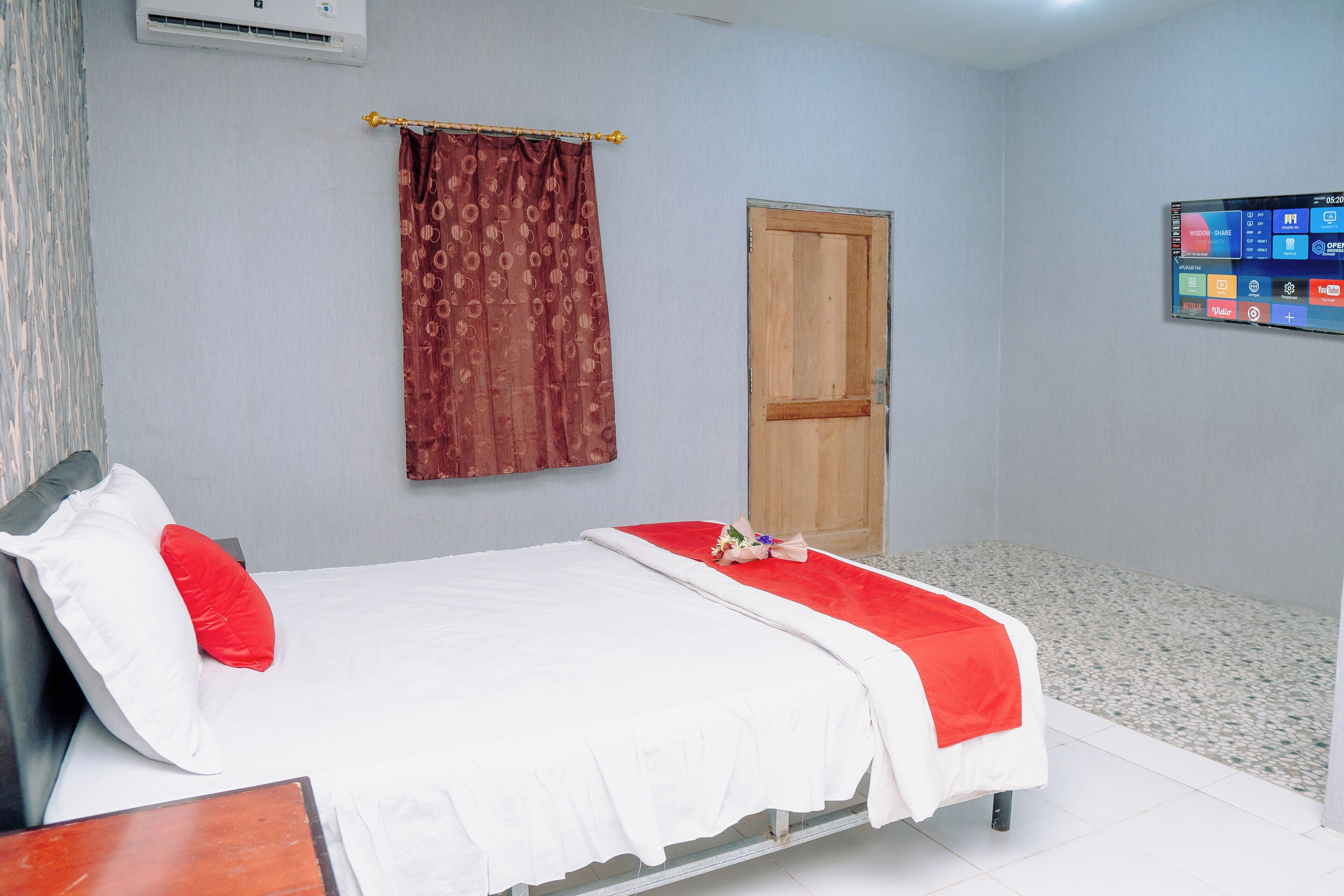 A neatly arranged bedroom with a bed, a wooden door, a wall-mounted air conditioner, and a digital display.